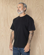 Man turned to the side, wearing a black Mock Neck t-shirt against a wood background. Model is 5'11", 198lbs wearing size L