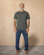 Man wearing a Steel Grey Pocket t-shirt and jeans against a wood background. Model is 5'11", 198lbs wearing size L