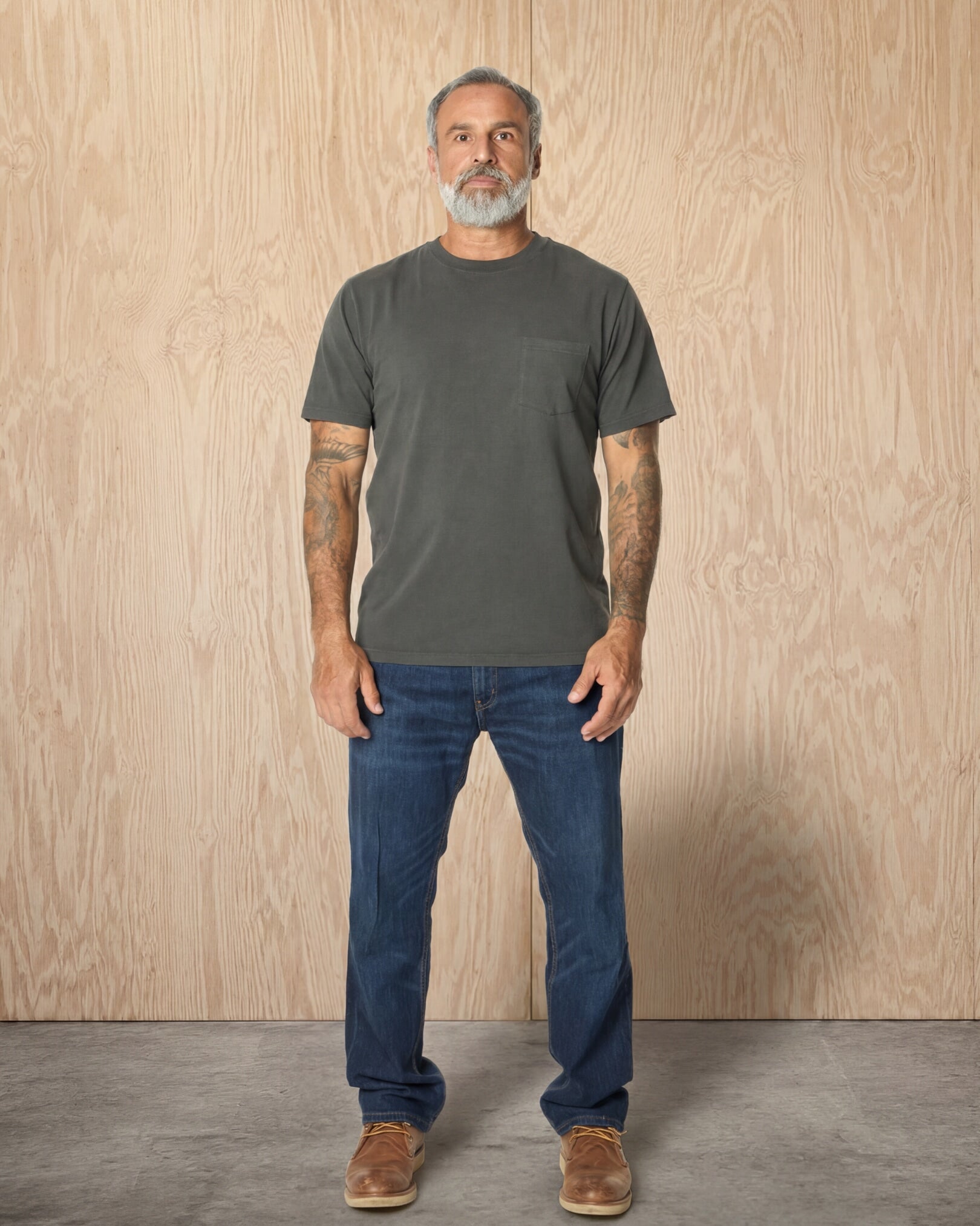 Man wearing a Steel Grey Pocket t-shirt and jeans against a wood background. Model is 5'11", 198lbs wearing size L
