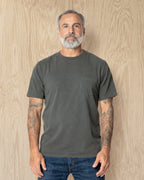 Man wearing a Steel Grey Pocket t-shirt and jeans against a wood background. Model is 5'11", 198lbs wearing size L