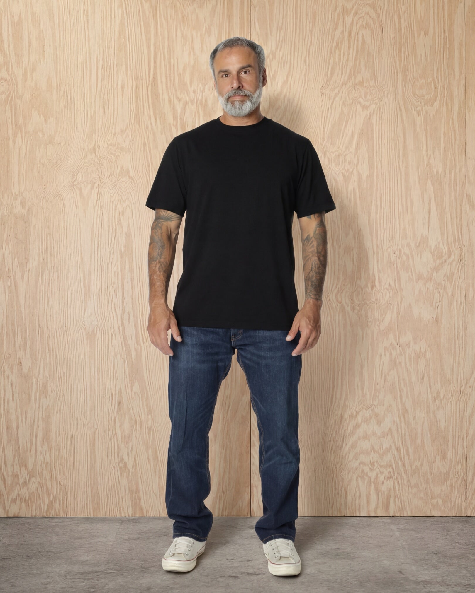 Man full body, wearing a black Premium t-shirt against a wood background. Model is 5'11", 198lbs wearing size L