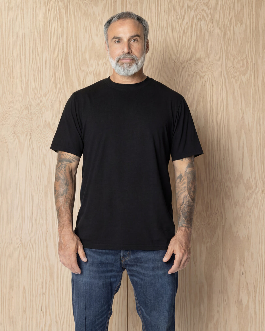 Man wearing a black Premium t-shirt against a wood background. Model is 5'11", 198lbs wearing size L