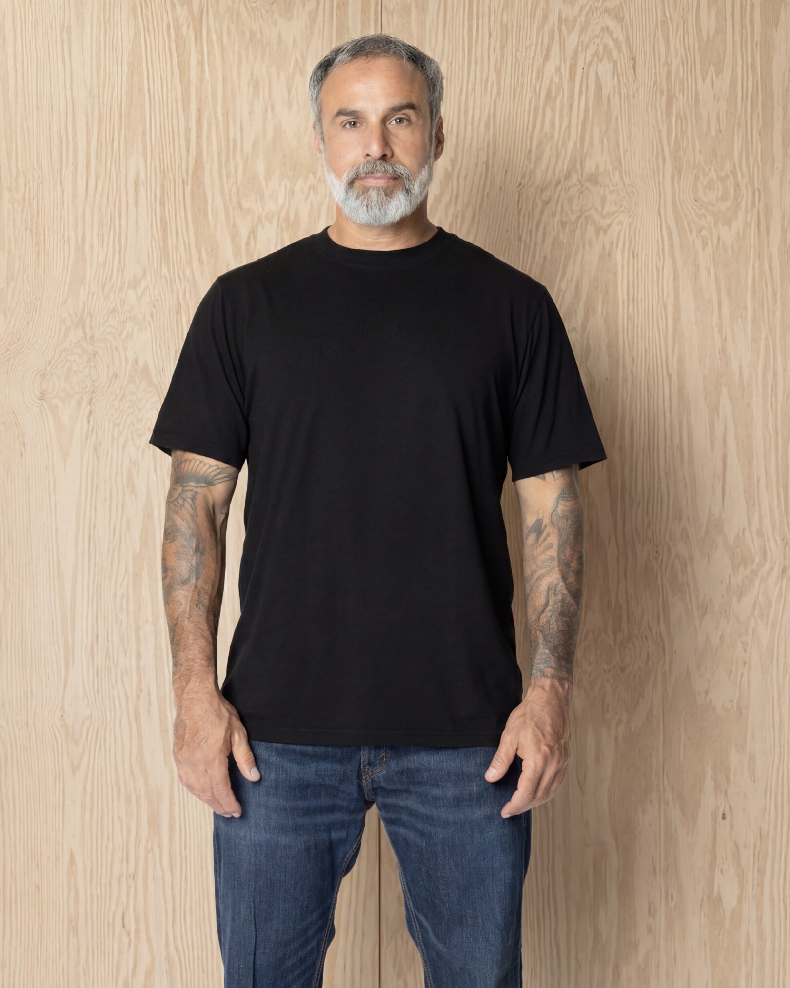 Man wearing a black Premium t-shirt against a wood background. Model is 5'11", 198lbs wearing size L