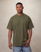 Man wearing an military green drop shoulder t-shirt against a beige background. Model is 6'0" wearing size L