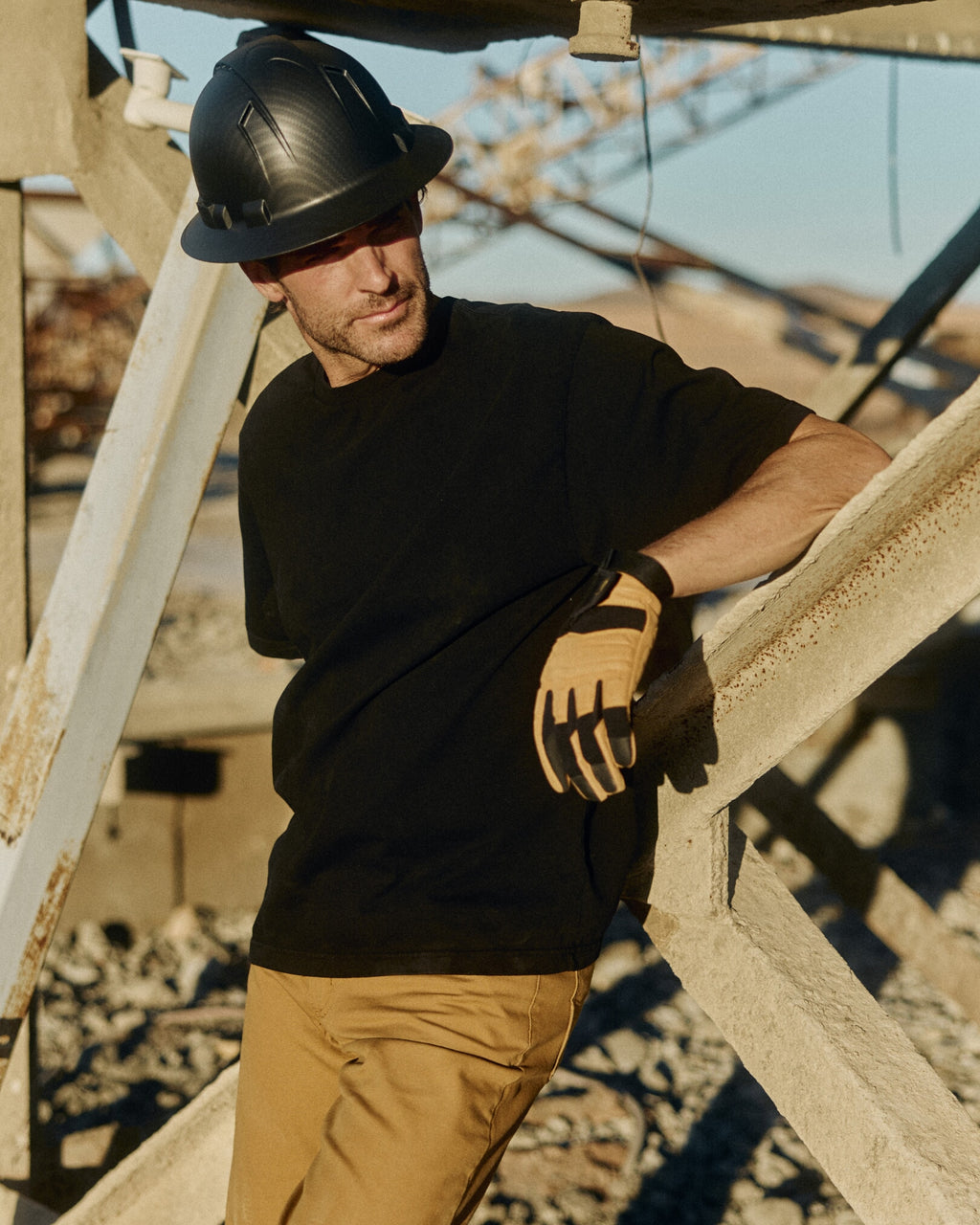 Man wearing a black hard hat and gloves standing on a construction site. Model is 6'1", 170lbs wearing size L