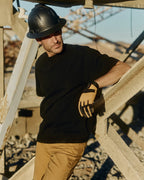 Man wearing a black hard hat and gloves standing on a construction site. Model is 6'1", 170lbs wearing size L