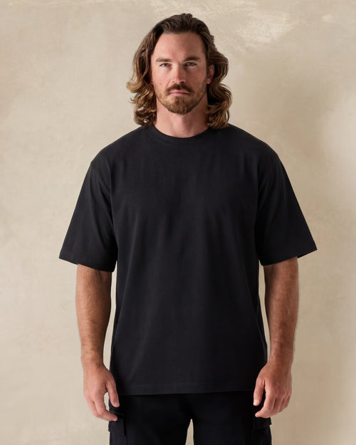Man wearing a black t-shirt against a beige background. Model is 6'1", 200lbs wearing size L