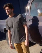 Man standing next to a truck wearing a steel grey pocket tee. Model is 6'1", 170lbs wearing size L