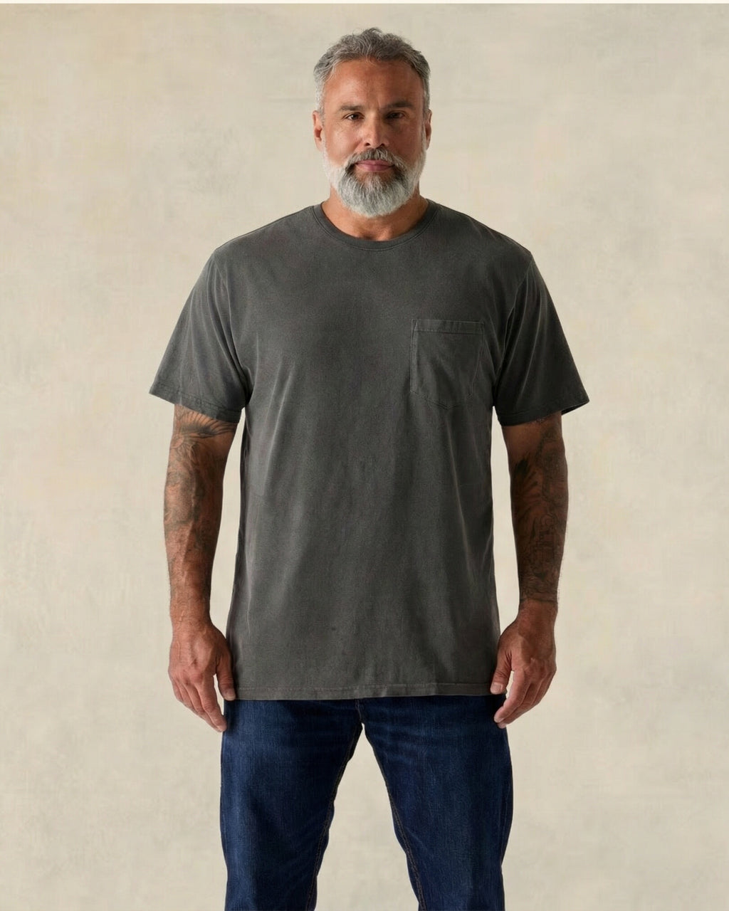 Man wearing a dark gray t-shirt and blue jeans against a beige background. Model is 5'11", 210lbs wearing size XL