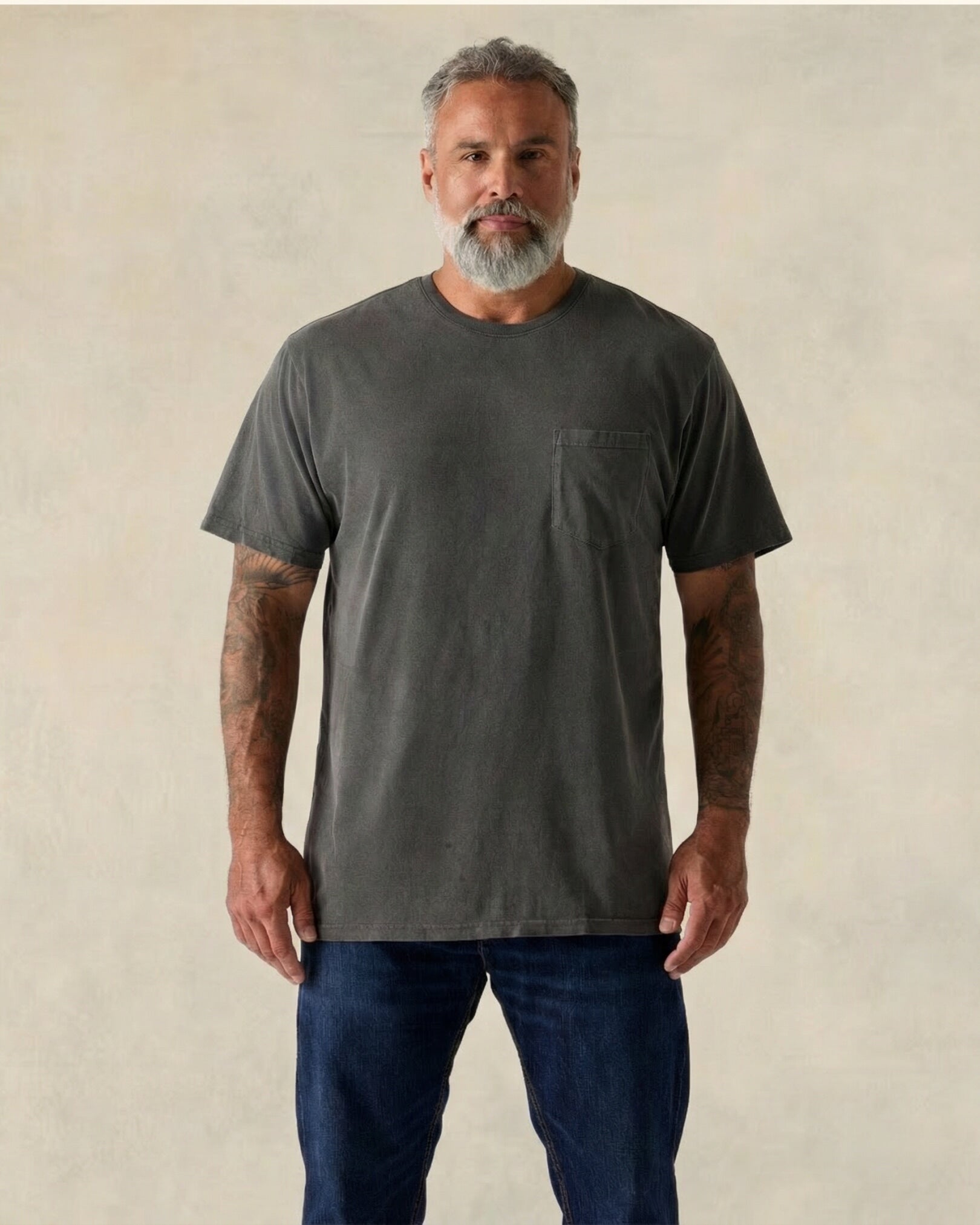 Man wearing a dark gray t-shirt and blue jeans against a beige background. Model is 5'11", 210lbs wearing size XL