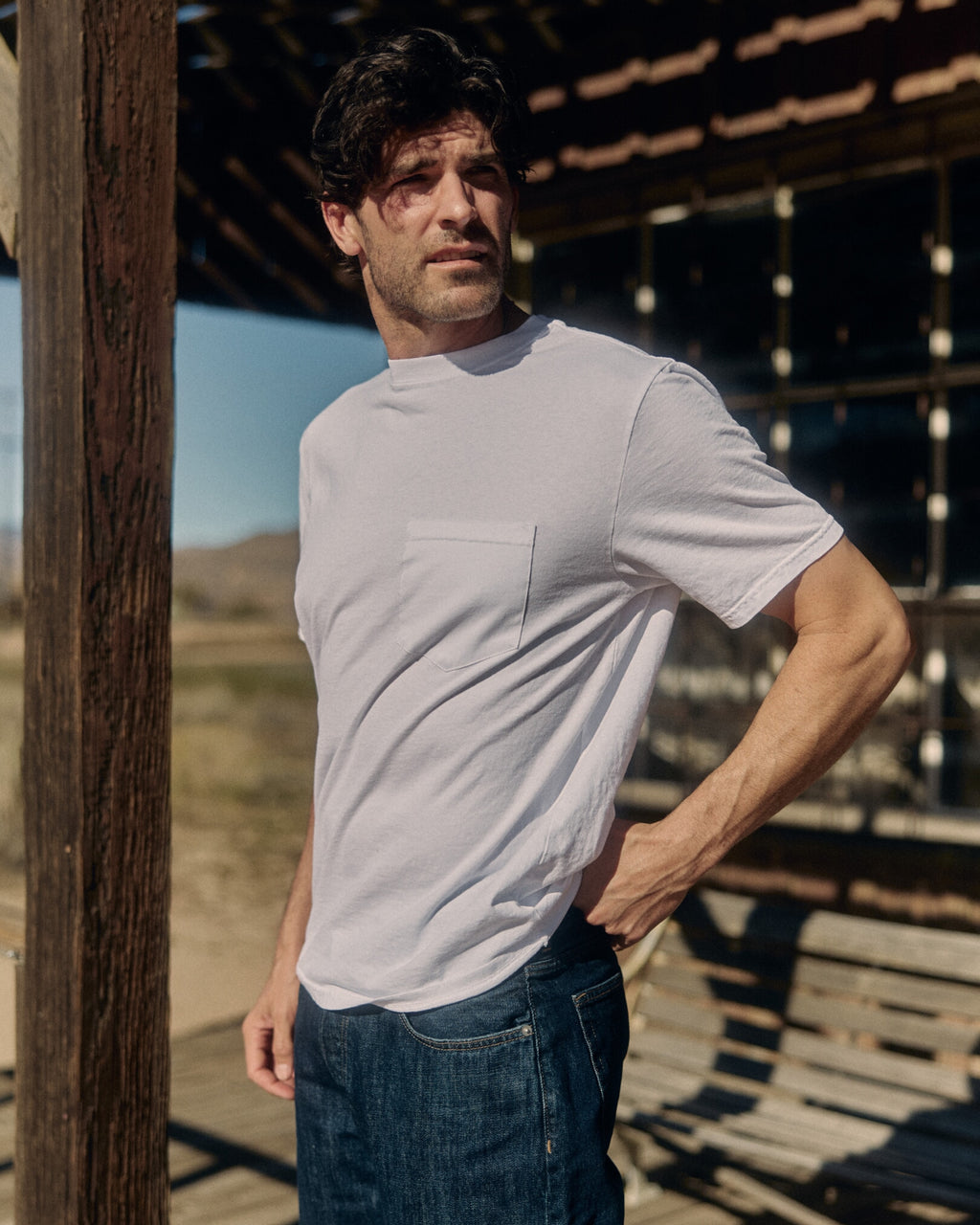 Man wearing a white t-shirt and blue jeans standing outdoors. Model is 6'1", 170lbs wearing size L