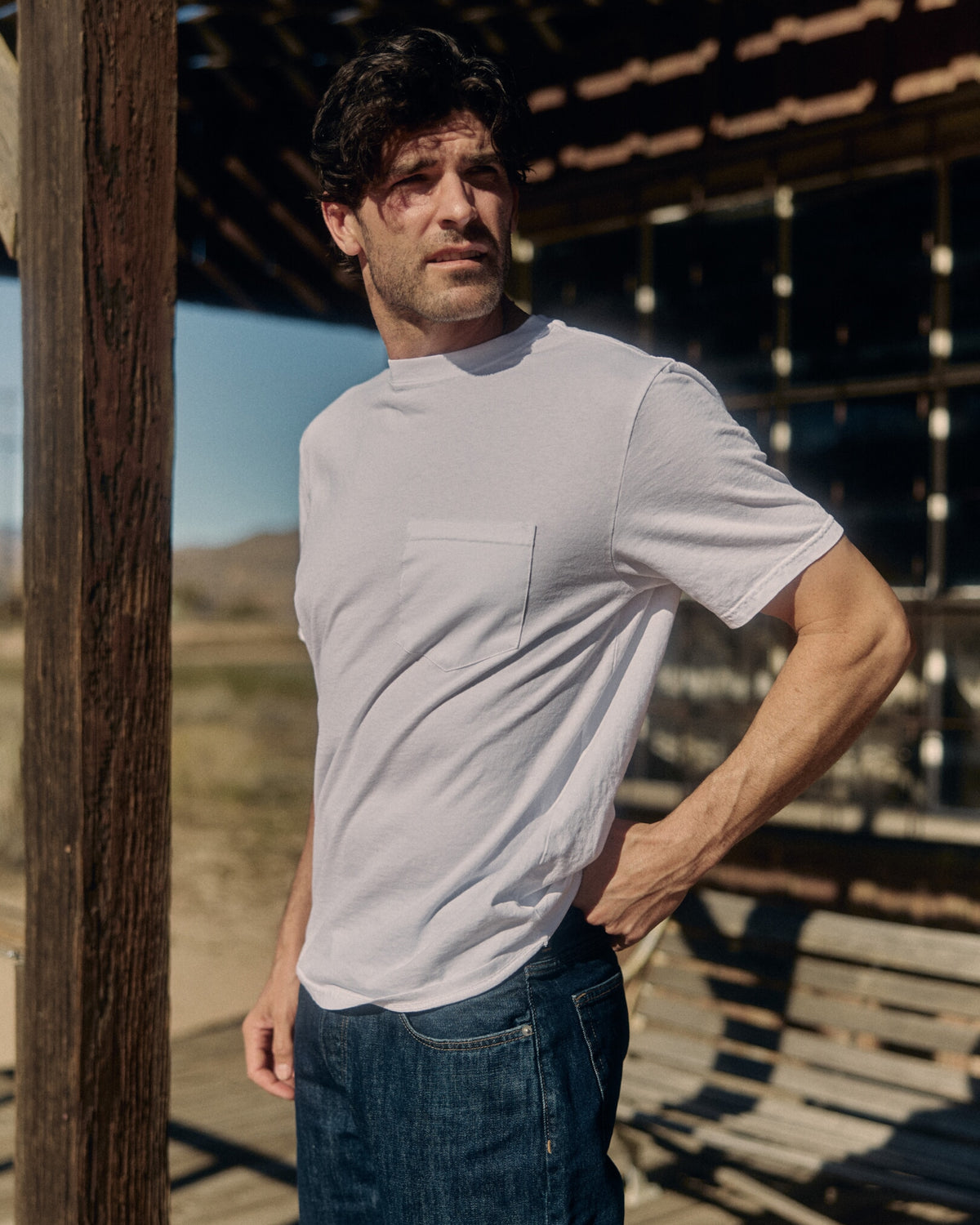 Man wearing a white t-shirt and blue jeans standing outdoors. Model is 6'1", 170lbs wearing size L