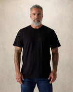Man wearing a black t-shirt against a beige background. Model is 5'11", 210lbs wearing size XL